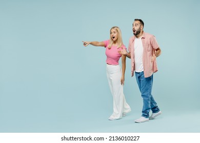 Full body young astonished couple two friends family surprised man woman 20s in casual clothes point finger aside on workspace together isolated on pastel plain light blue background studio portrait.