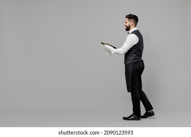 Full Body Young Barista Male Waiter Butler Man 20s Wear White Shirt Vest Elegant Uniform Work At Cafe Give Bottle Of Wine Isolated On Plain Grey Background Studio Portrait. Restaurant Employee Concept