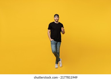 Full body young bearded tattooed man 20s he wears casual black t-shirt cap hold takeaway delivery craft paper brown cup coffee to go isolated on plain yellow wall background. People lifestyle concept - Powered by Shutterstock