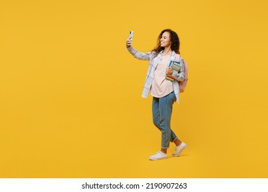 Full Body Young Black Teen Girl Student She Wear Casual Clothes Backpack Bag Hold Books Do Selfie Shot On Mobile Cell Phone Isolated On Plain Yellow Background. High School University College Concept