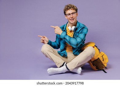 Full Body Young Boy Teen Student Wear Casual Clothes Backpack Headphones Glasses Sit Point Finger Aside On Workspace Area Isolated On Violet Background Studio Education In University College Concept