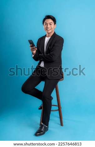 Full body Young business man wearing a vest using phone and posing on a blue background