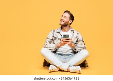 Full body young Caucasian man he wears brown shirt casual clothes sitting hold in hand use mobile cell phone look aside isolated on plain yellow orange background studio portrait. Lifestyle concept - Powered by Shutterstock