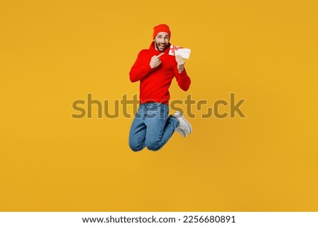 Full body young caucasian man wear red hoody hat hold point finger on gift certificate coupon voucher card for store isolated on plain yellow color background studio portrait. People lifestyle concept