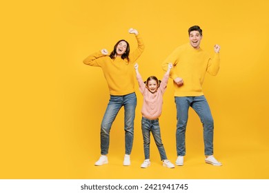 Full body young cheerful cool happy parents mom dad with child kid girl 7-8 years old wear pink sweater casual clothes dancing posing have fun isolated on plain yellow background. Family day concept