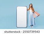 Full body young cheerful woman wear casual clothes hold shopping paper package bags big huge blank screen area mobile cell phone isolated on plain blue background. Black Friday sale buy day concept