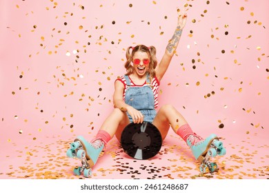 Full body young cool disc jockey DJ woman wear red t-shirt denim overalls casual clothes blue rollers rollerblading hold vinyl disk show v-sign isolated on plain pink background. Summer sport concept