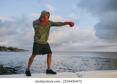 Full body young cool strong sporty athletic toned fit sportsman man wears sports clothes red gloves boxing warm up training at sunrise sun dawn over sea beach outdoor on seaside in summer day morning - Powered by Shutterstock