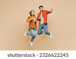 Full body young couple two friends family man woman wear casual clothes together doing selfie shot on mobile cell phone post photo on social network jump high isolated on pastel plain beige background