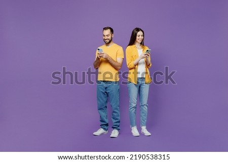 Full body young couple two friends family man woman together in yellow casual clothes hold in hand use mobile cell phone browsing internet chatting online isolated on plain violet background studio