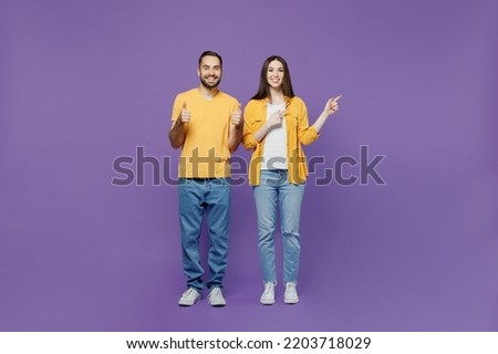 Full body young couple two friends family man woman together in yellow casual clothes point index finger aside on workspace area mock up copy space isolated on plain violet background studio portrait