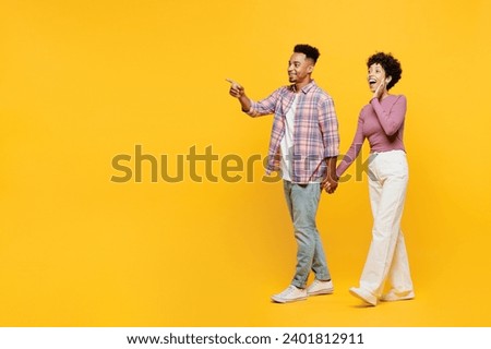 Full body young couple two friend family man woman of African American ethnicity wear purple casual clothes together walk go stroll point index finger aside on area isolated on plain yellow background