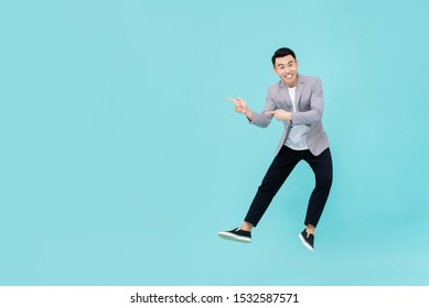 Full body of young dynamic handsome smiling Asian man in smart casual business clothes jumping and pointing fingers to copy space isolated on light blue background - Powered by Shutterstock