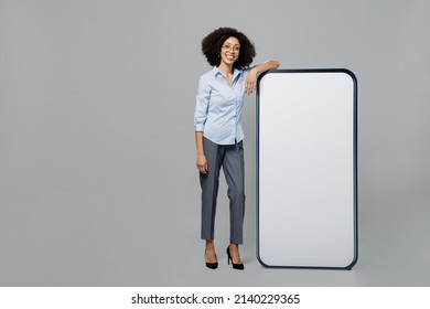 Full Body Young Employee Business Corporate Lawyer Woman Of African American Ethnicity In Shirt Work In Office Near Big Blank Screen Mobile Cell Phone Workspace Mockup Area Isolated On Grey Background