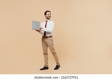 Full Body Young Employee Business Man Corporate Lawyer 20s Wear White Shirt Red Tie Glasses Work In Office Hold Use Laptop Pc Computer Look Aside On Worspace Area Isolated On Plain Beige Background