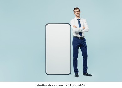 Full body young employee IT business man corporate lawyer wear classic formal shirt tie work in office stand near big huge blank screen mobile cell phone with area isolated on plain blue background - Shutterstock ID 2313389467