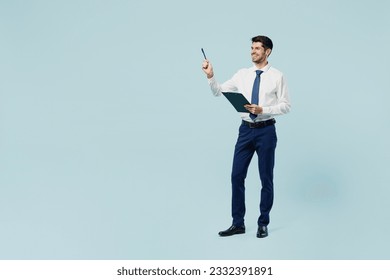 Full body young employee IT business man corporate lawyer wears classic formal shirt tie work in office hold clipboard with paper account documents point pen aside isolated on plain blue background