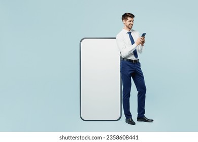 Full body young employee IT business man corporate lawyer in classic formal shirt tie work in office big huge blank screen mobile cell phone with area use smartphone isolated on plain blue background - Powered by Shutterstock