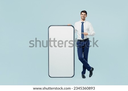 Full body young employee business man corporate lawyer wear classic formal shirt work in office point on big huge blank screen mobile cell phone smartphone with area isolated on plain blue background