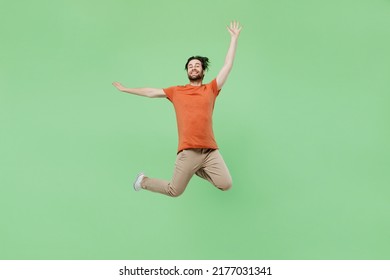 Full body young excited fun cool man 20s wear casual orange t-shirt jump high with outsretched hands isolated on plain pastel light green color background studio portrait. People lifestyle concept.