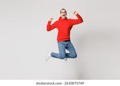 Cuerpo completo joven emocionado overjoyed hombre de Oriente Medio vestido rojo con capucha ropa casual saltar alto hacer ganador gesto apriete el puño aislado en el fondo blanco sólido liso retrato de estudio. Concepto de estilo de vida