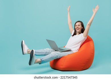 Full body young excited woman 20s she wear white t-shirt sit in bag chair hold use work on laptop pc computer raise up hands finish job celebrate isolated on plain pastel light blue cyan background - Shutterstock ID 2217547345