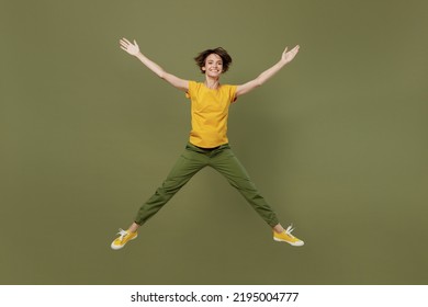 Full body young exultant fun happy woman she 20s wear yellow t-shirt jump high with outstretched hands legs like flying in air isolated on plain olive green khaki background. People lifestyle concept