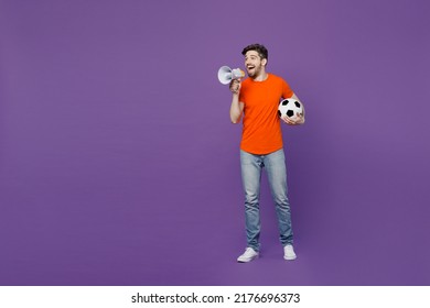 Full Body Young Fan Man He Wear Orange T-shirt Cheer Up Support Football Sport Team Hold Soccer Ball Watch Tv Live Stream Scream Megaphone Announces Hurry Up Isolated On Plain Dark Purple Background