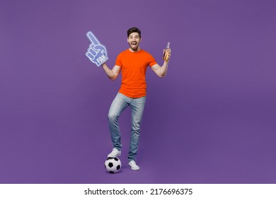 Full Body Young Fan Man He Wear Orange T-shirt Cheer Up Support Football Sport Team Hold Soccer Ball Fan Foam Glove Finger Up Beer Bottle Watch Tv Live Stream Isolated On Plain Dark Purple Background