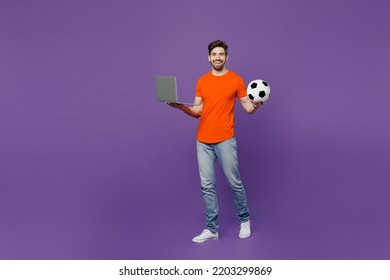 Full body young fan man wear orange t-shirt cheer up support football sport team hold soccer ball watch tv live stream 2024 use betting on laptop pc computer isolated on plain dark purple background - Shutterstock ID 2203299869