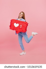 Full body young female in casual outfit smiling and holding speech bubble with like icon while advertising social media against pink background - Shutterstock ID 1513619135