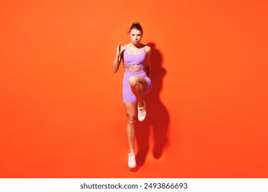 Full body young fitness trainer instructor woman sportsman wear top shorts purple clothes train in home gym jump high run look camera isolated on plain orange background. Workout sport fit abs concept - Powered by Shutterstock