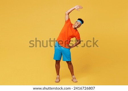 Full body young fitness trainer sporty man sportsman wear orange t-shirt do stretch lunge exercise rising hands up train in home gym isolated on plain yellow background. Workout sport fit abs concept