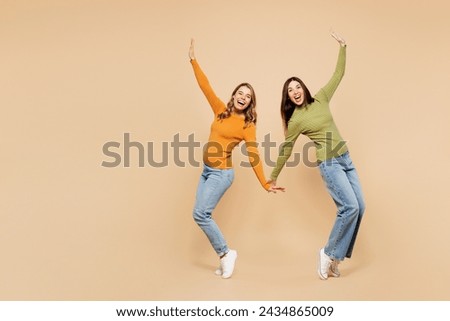 Full body young friends two women wear orange green shirt casual clothes together stand on toes with outstretched hands leaning back dance posing isolated on plain beige background. Lifestyle concept