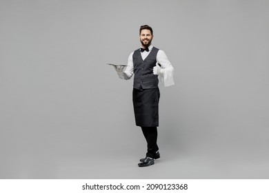 Full Body Young Fun Barista Male Waiter Butler Man Wear White Shirt Vest Elegant Uniform Work At Cafe Hold Carry Metal Tray Show Thumb Up Isolated On Plain Grey Background Restaurant Employee Concept