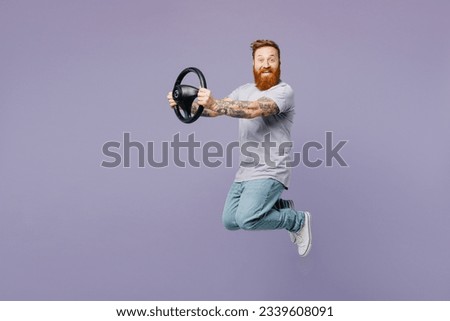 Full body young fun cheerful redhead bearded man wear violet t-shirt casual clothes hold steering wheel driving car jump high isolated on plain pastel light purple background studio. Lifestyle concept