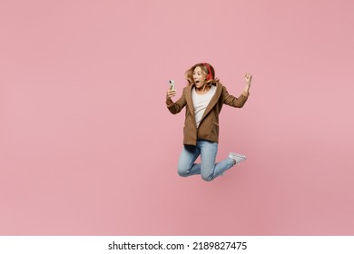 Full Body Young Fun Employee Business Woman 30s She Wear Casual Classic Jacket Headphones Listen Music Jump High Hold Mobile Cell Phone Do Winner Gesture Isolated On Plain Pastel Light Pink Background