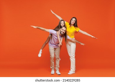 Full Body Young Fun Happy Parents Mom Dad With Child Kid Daughter Teen Girl In Basic T-shirts Giving Piggyback Ride To Joyful, Sit On Back Isolated On Yellow Background. Family Day Childhood Concept.