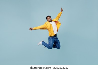 Full body young fun man of African American ethnicity 20s wear yellow shirt jump high with outstretched hands isolated on plain pastel light blue background studio portrait. People lifestyle concept