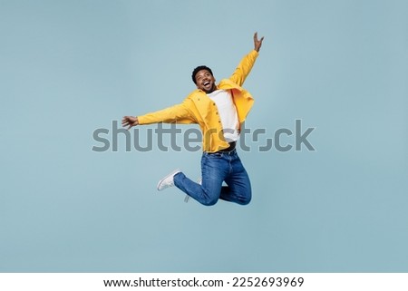 Full body young fun man of African American ethnicity 20s wear yellow shirt jump high with outstretched hands isolated on plain pastel light blue background studio portrait. People lifestyle concept