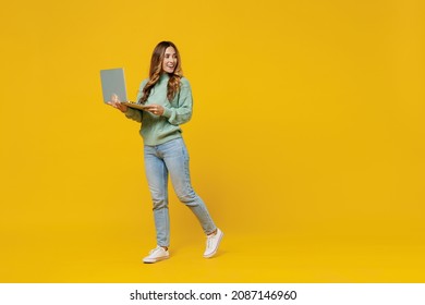 Full Body Young Fun Woman 30s In Green Knitted Sweater Hold Use Work On Laptop Pc Computer Look Aside On Copy Space Area Isolated On Plain Yellow Background Studio Portrait. People Lifestyle Concept