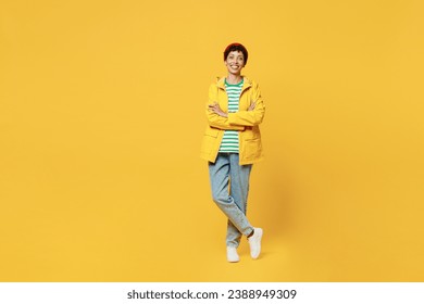 Full body young fun woman wears waterproof raincoat outerwear red hat hold hands crossed folded isolated on plain yellow background studio portrait. Outdoors lifestyle wet fall weather season concept - Powered by Shutterstock