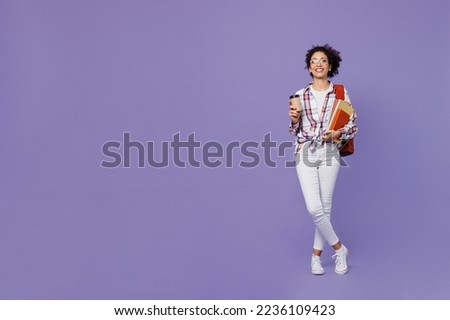 Full body young girl woman of African American ethnicity teen student in shirt hold takeaway delivery craft paper cup coffee to go isolated on plain purple background. Education in college concept.