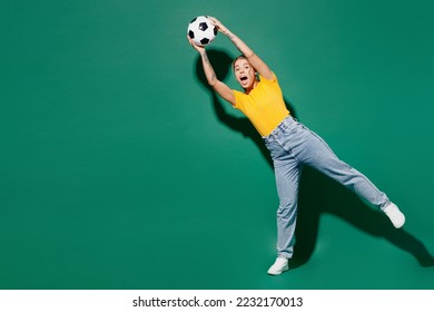 Full body young goalkeeper cheerful woman fan wearing basic yellow t-shirt cheer up support football sport team hold in hand catch soccer ball watch tv live stream isolated on dark green background - Powered by Shutterstock