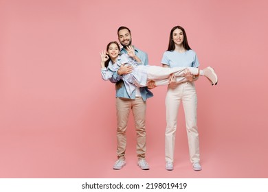 Full Body Young Happy Cherful Cool Parents Mom Dad With Child Kid Daughter Teen Girl In Blue Clothes Hold Kid Look Camera Show Ok Isolated On Plain Pastel Light Pink Background. Family Day Concept.