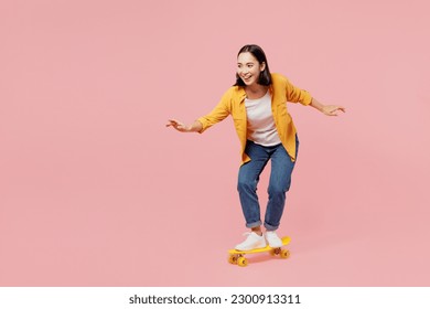 Full body young happy fun cool woman of Asian ethnicity wear yellow shirt white t-shirt riding skateboard pennyboard isolated on plain pastel light pink background studio portrait. Lifestyle concept - Powered by Shutterstock