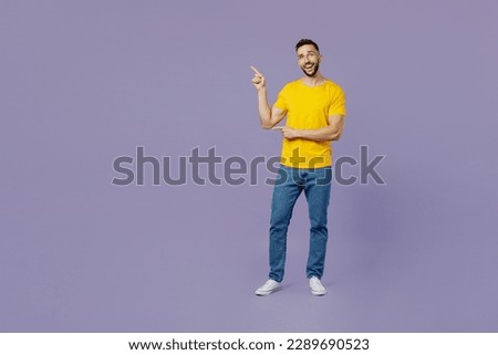Full body young happy fun cool caucasian man wear yellow t-shirt point index finger aside indicate on workspace area copy space mock up isolated on plain pastel light purple background studio portrait