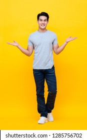 Full Body Of Young Happy Handsome Asian Man Raising His Hands With Open Palms Gesture Studio Shot Isolated On Colorful Yellow Background