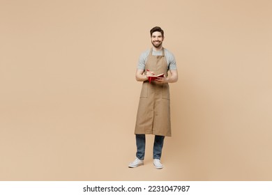 Full body young happy man barista barman employee wear brown apron work in coffee shop write down order menu in notebook isolated on plain pastel light beige background. Small business startup concept - Powered by Shutterstock