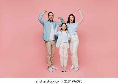 Full Body Young Happy Overjoyed Parents Mom Dad With Child Kid Daughter Teen Girl In Blue Clothes Doing Winner Gesture Celebrate Clenching Fists Say Yes Isolated On Plain Pastel Light Pink Background.